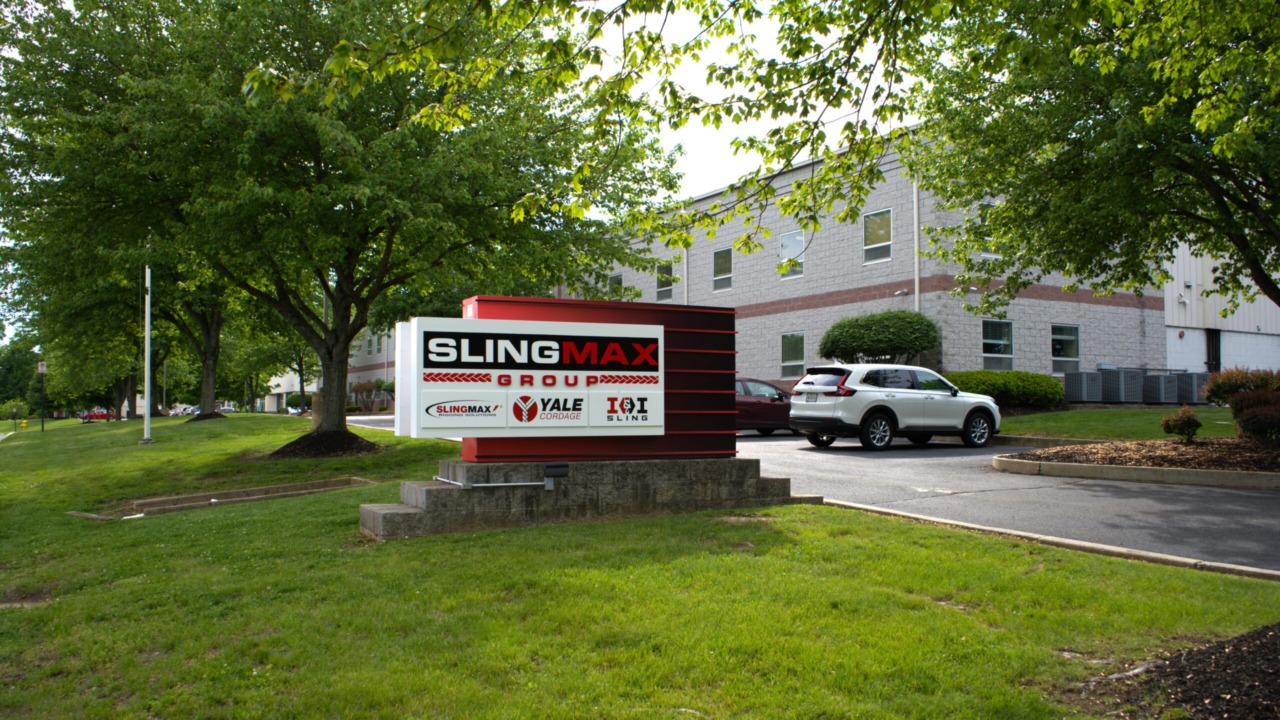 SlingMax Group building exterior with company sign, cars parked outside, surrounded by trees and greenery.