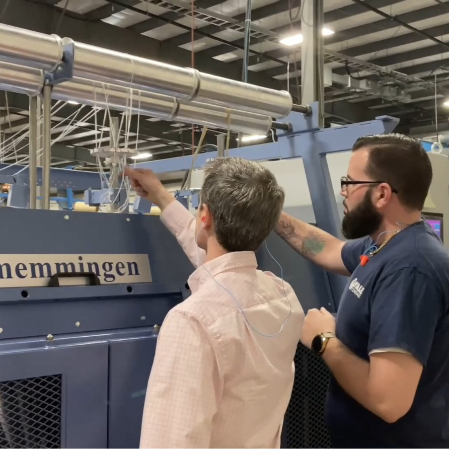 Two men operating a large industrial machine in a factory setting, focusing on controls and adjustments.