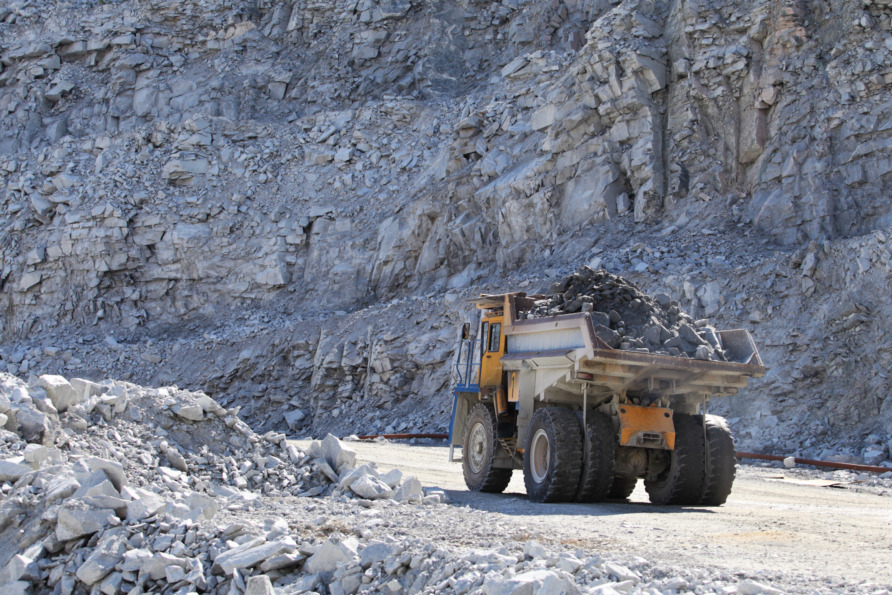 Dump truck loaded with rocks in a quarry with rocky cliff in the background.