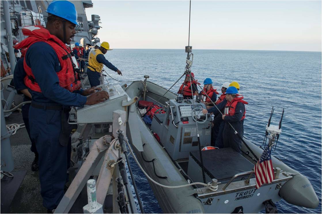 Crew members prepare and launch a small boat from a large ship into the ocean during a maritime operation exercise.