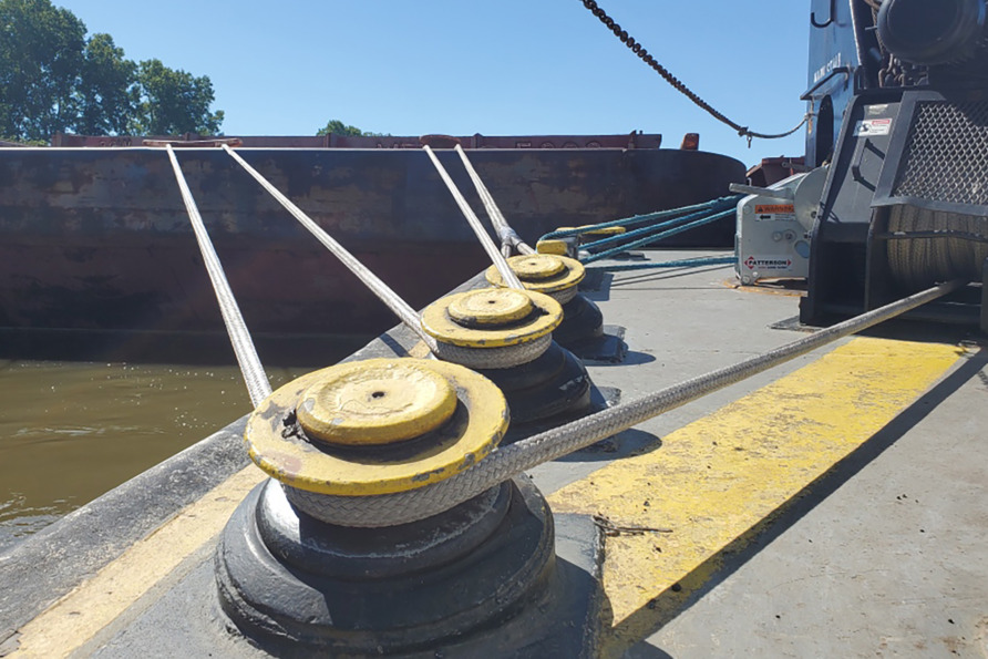 A docked barge secured with yellow bollards and taut ropes under a clear blue sky.