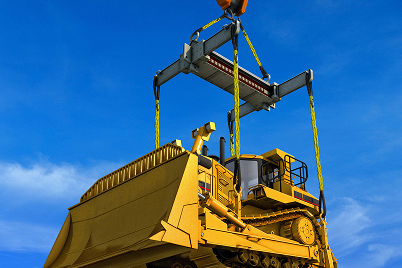 Bulldozer being lifted by crane with bright blue sky in the background