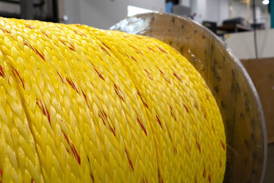 large spool of bright yellow braided rope with red accents in an industrial setting