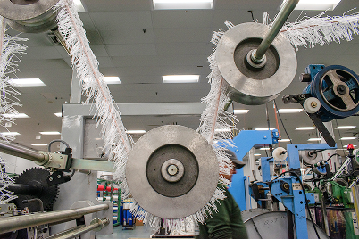 Factory textile machine with multiple rollers and fabric strands being processed in an industrial setting.