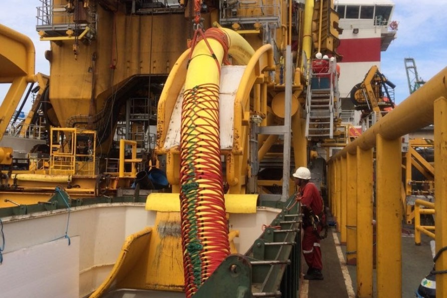Engineer inspecting large industrial machinery on an offshore oil rig deck with yellow and red equipment around.