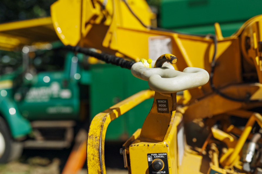 Close-up of a yellow construction crane's winch hook with a blurred green truck in the background.