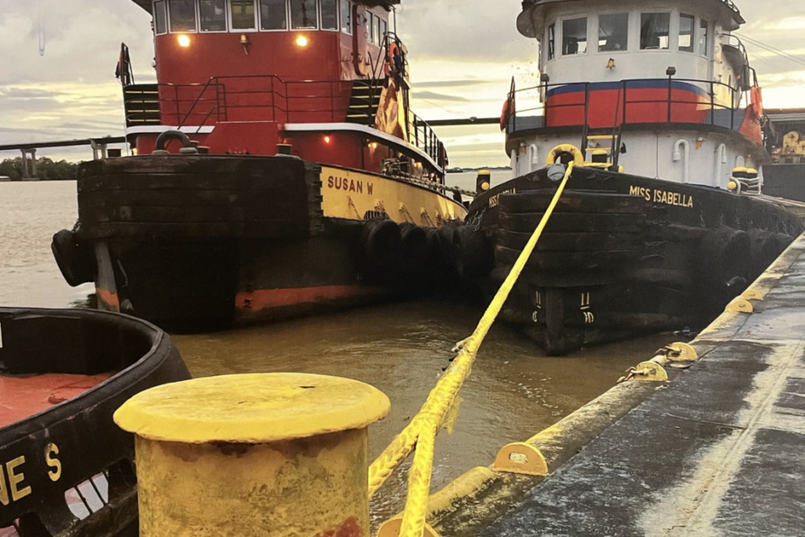Two tugboats docked at a pier, secured with a yellow rope, against a cloudy sky backdrop.