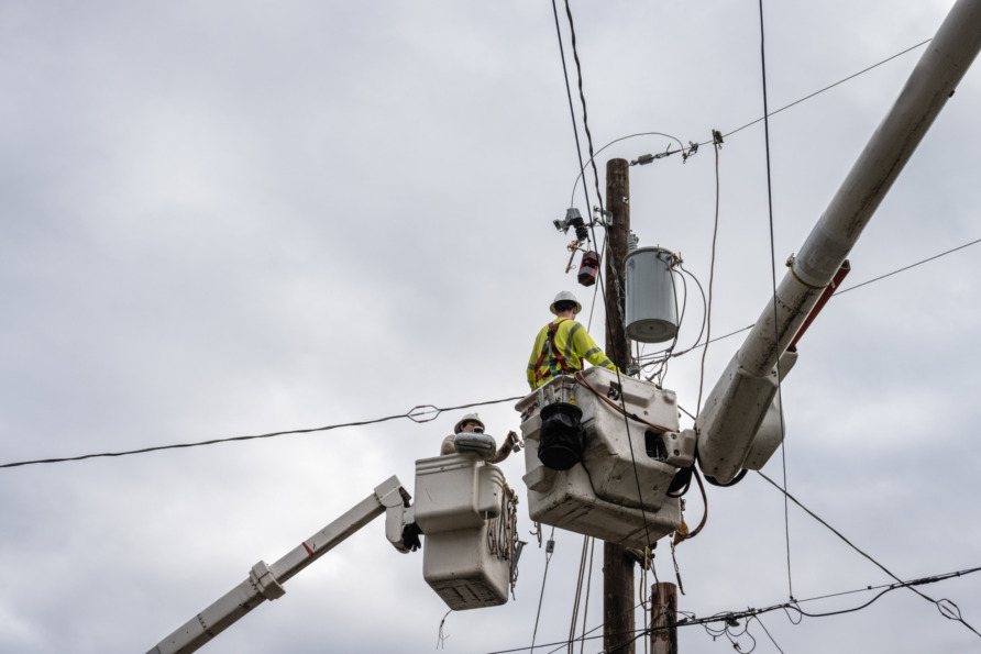 Workers in bucket trucks repairing electrical power lines against cloudy sky.