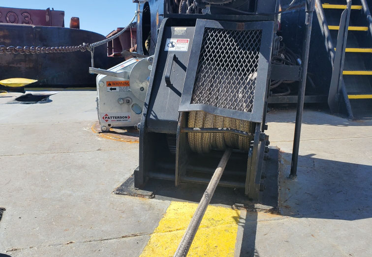 Industrial equipment with cables on a ship deck, featuring a winch and yellow safety markings.