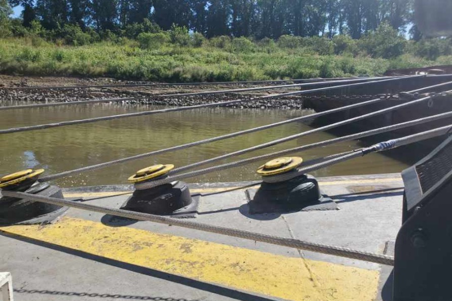 Barge mooring cables secured at concrete bollards, in river setting with trees lining the distant bank.