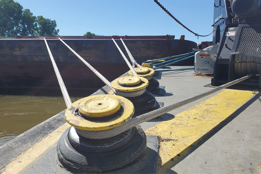 Ropes tied to bollards on a dock, securing a large barge in the water under a clear blue sky.