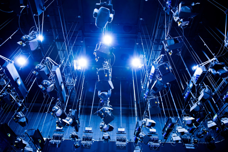 Stage lighting setup with multiple hanging spotlights and blue illumination in a theatrical or studio environment.