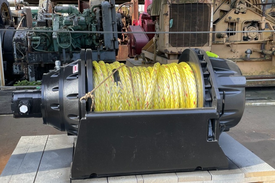 Industrial winch with yellow rope, placed on a wooden pallet in a machinery workshop setting.