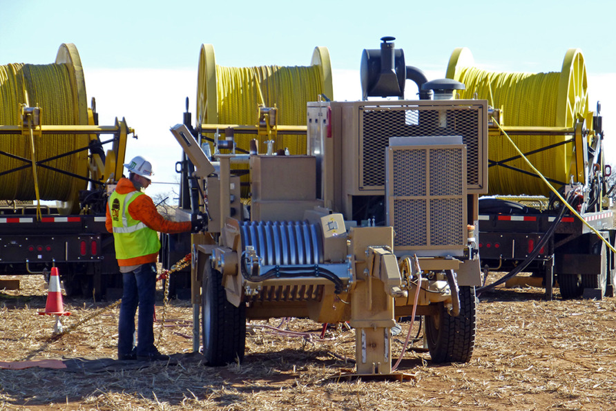 Worker operating heavy machinery near large spools of yellow cable on a construction site.