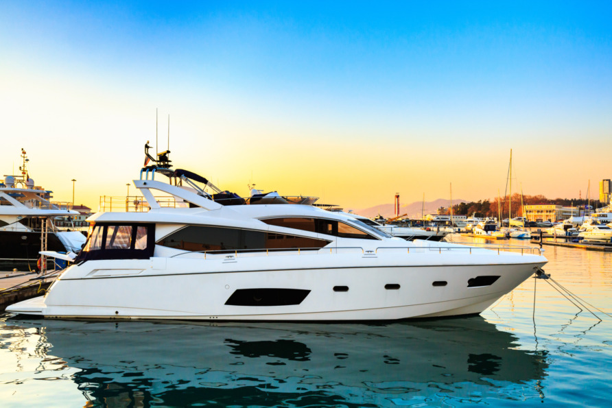Luxury yacht docked at marina during sunset with other boats and calm water reflecting the colorful sky.