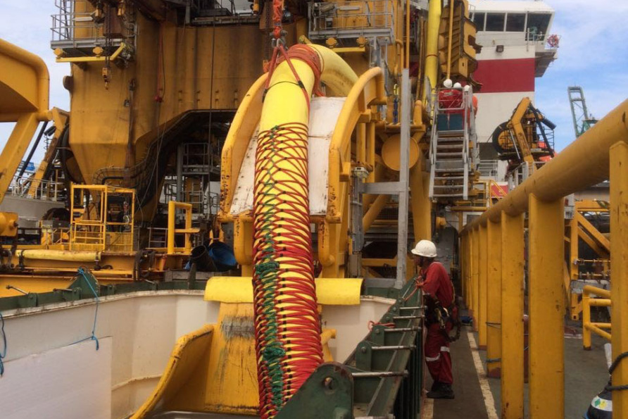 Worker in protective gear stands near industrial machinery on a large offshore equipment platform.