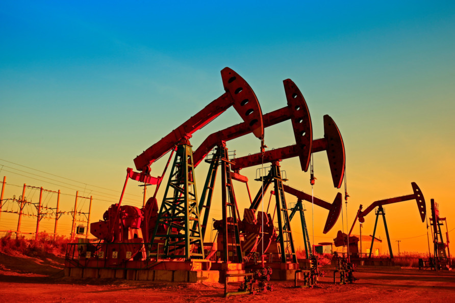 Oil pumpjacks operating at sunset in a remote field with vibrant orange and blue sky in the background.