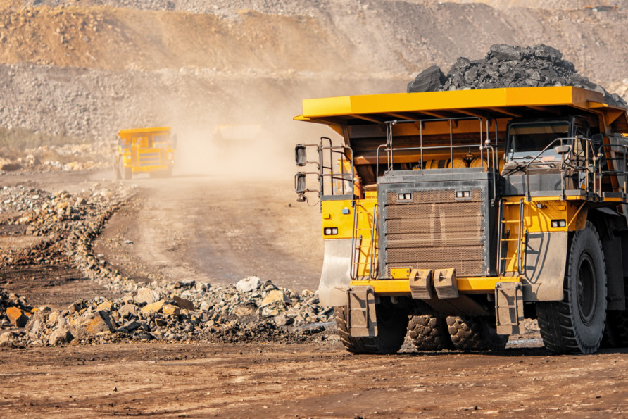 Large mining trucks transporting materials in an open-pit mine, driving on dusty paths with rocky backgrounds.