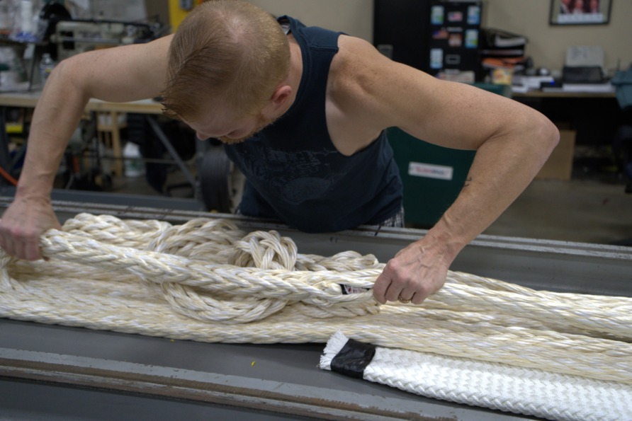 Person inspecting large coiled rope in a workshop setting.