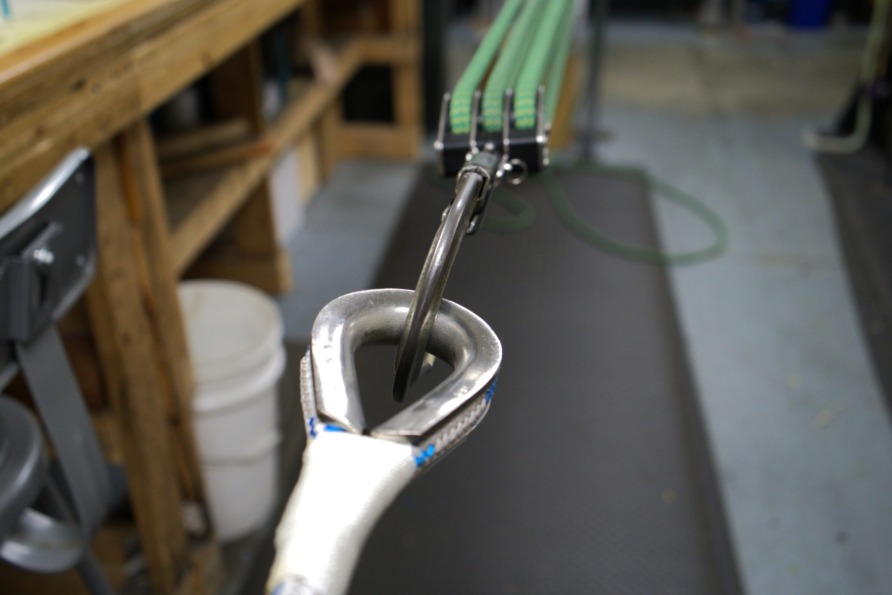 Close-up of a tensioned spring in a workshop, showing metal loops and green bands on a workbench background.