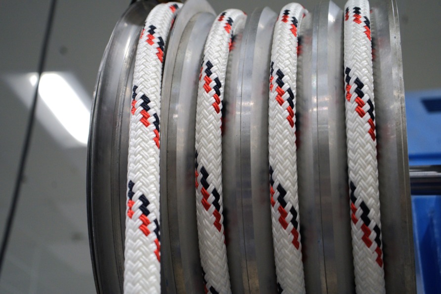 Close-up of a white and patterned rope coiled on a metallic spool in an industrial setting.