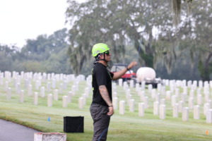 Arborist in a helmet working at a cemetery, surrounded by gravestones and trees in the background.