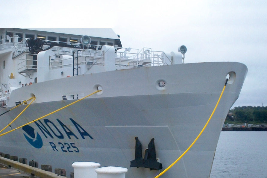 NOAA research vessel R-225 docked at a port, moored with yellow ropes, with overcast sky background.