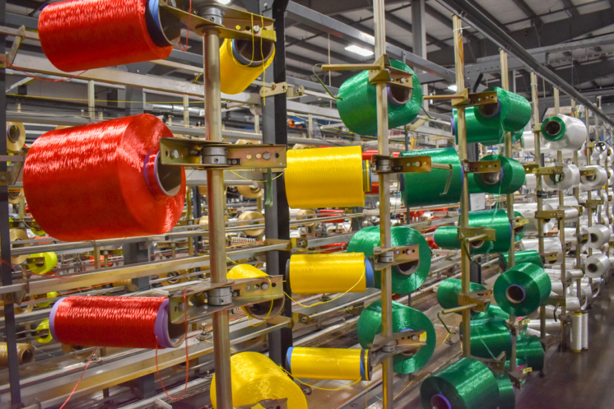 Spools of colorful textile threads in a manufacturing factory with red, yellow, and green threads in rows.
