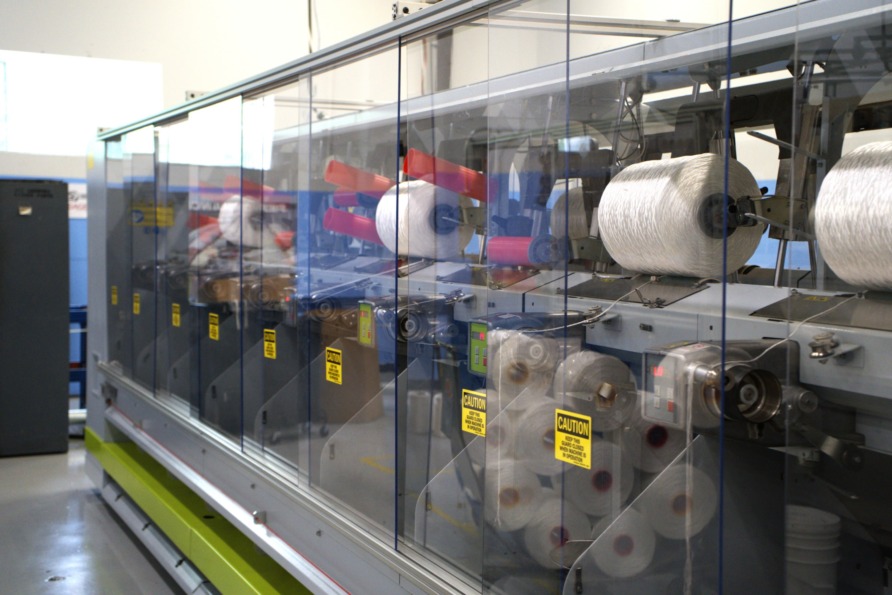 Industrial textile machine with spools of white thread in a manufacturing facility.