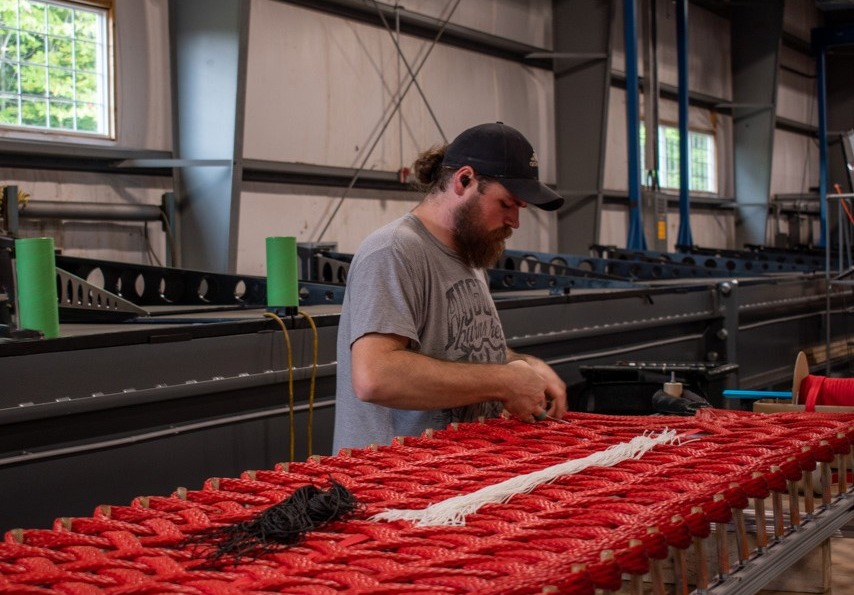 Man working on red ropes in an industrial setting with machinery and windows in the background.