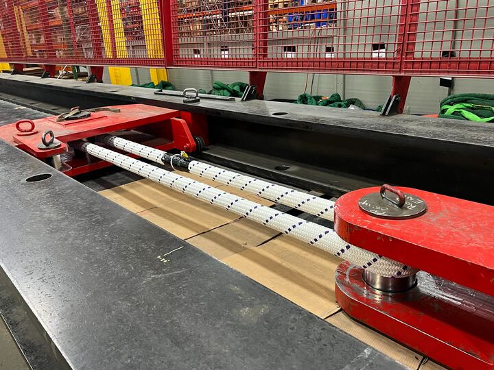 Close-up of industrial machinery with red components and a secured cable under a metal frame.