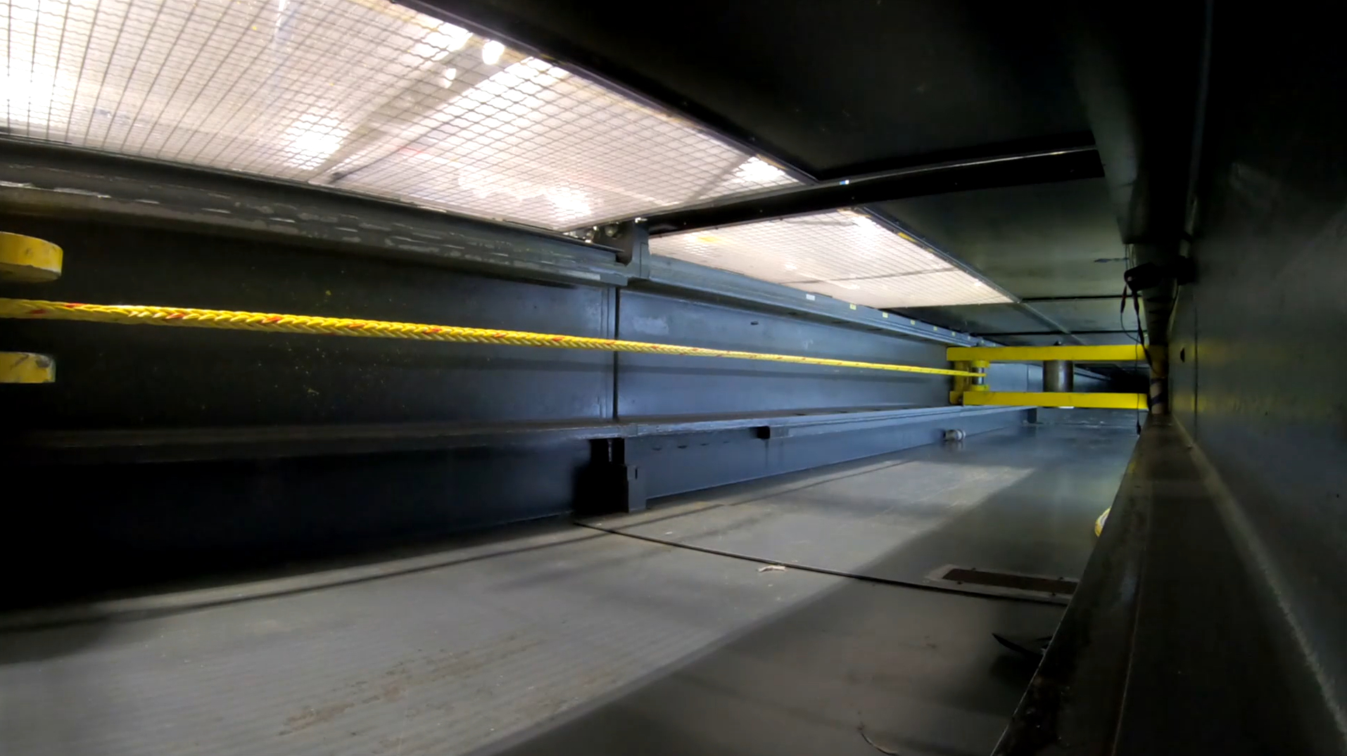 Interior view of an empty industrial container with yellow hooks and metal walls, light filtering through the top mesh.