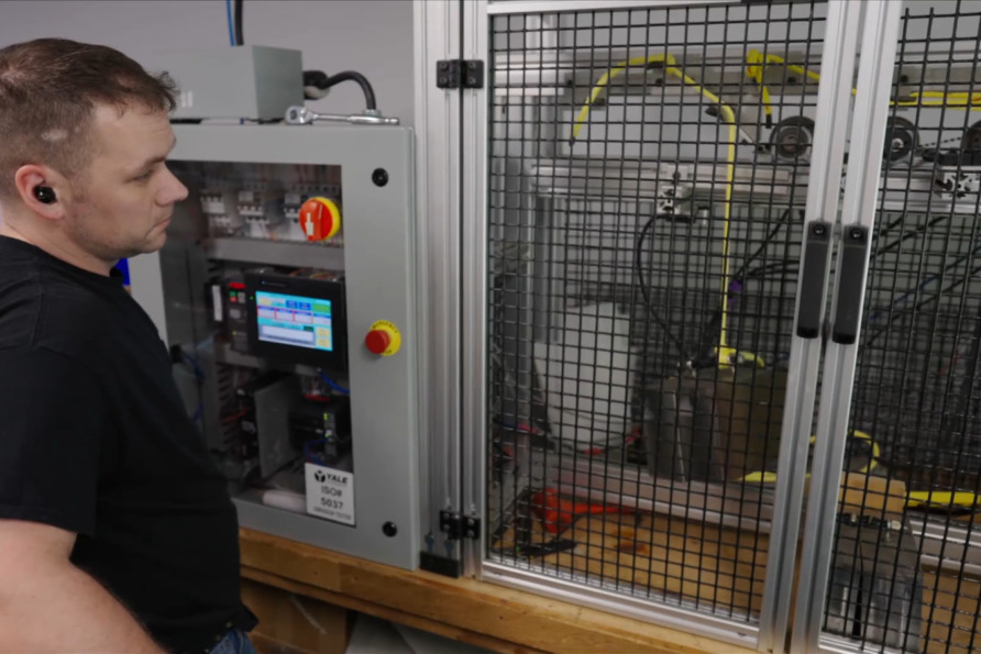 Man observing machinery with control panel and wires in a workshop setting.