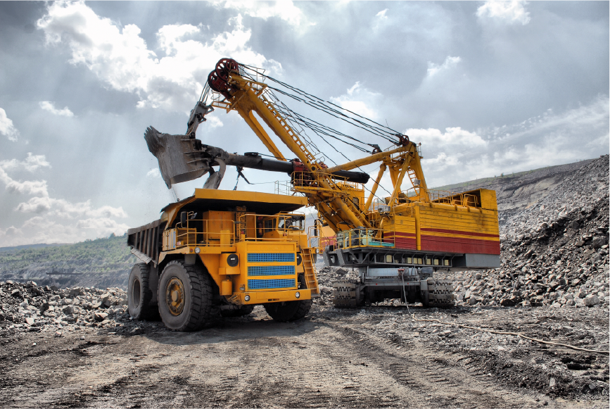 Excavator loading rocks into a dump truck at a mining site under a cloudy sky.