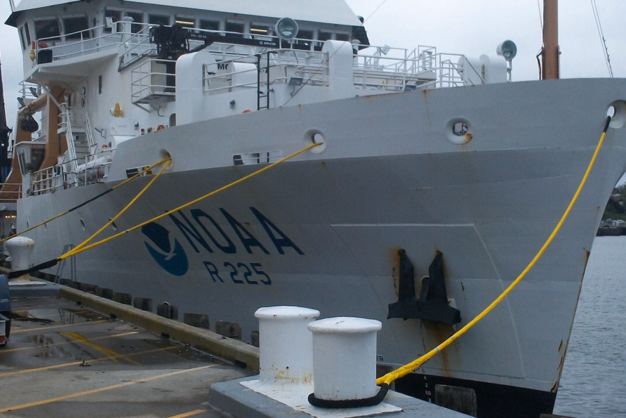 NOAA research ship R 225 docked at a harbor with yellow ropes securing it to the pier.