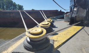 Boat mooring lines secured to bollards on a sunny day, with a view of the river and trees in the background.