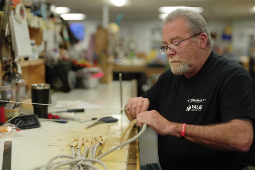 Man at workbench crafting rope products with tools and materials in workshop environment.