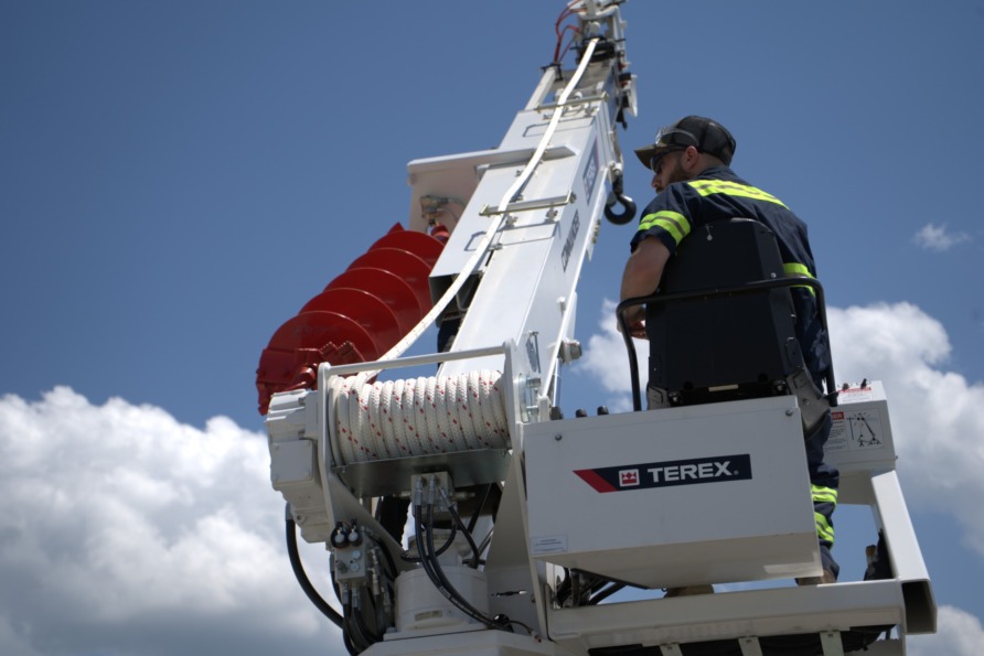 Worker operating a Terex construction lift against a clear blue sky with white clouds.