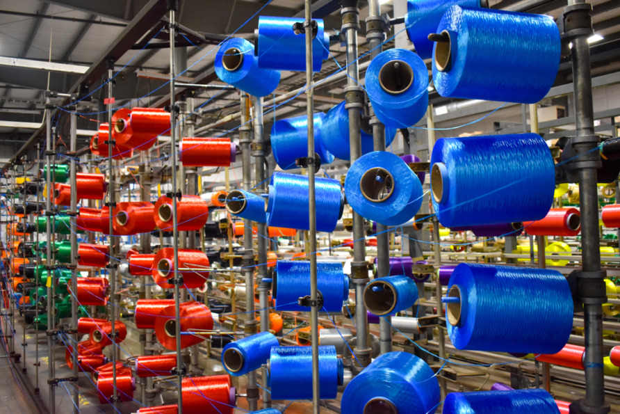 Brightly colored industrial spools of red, blue, and green thread in a textile manufacturing facility.
