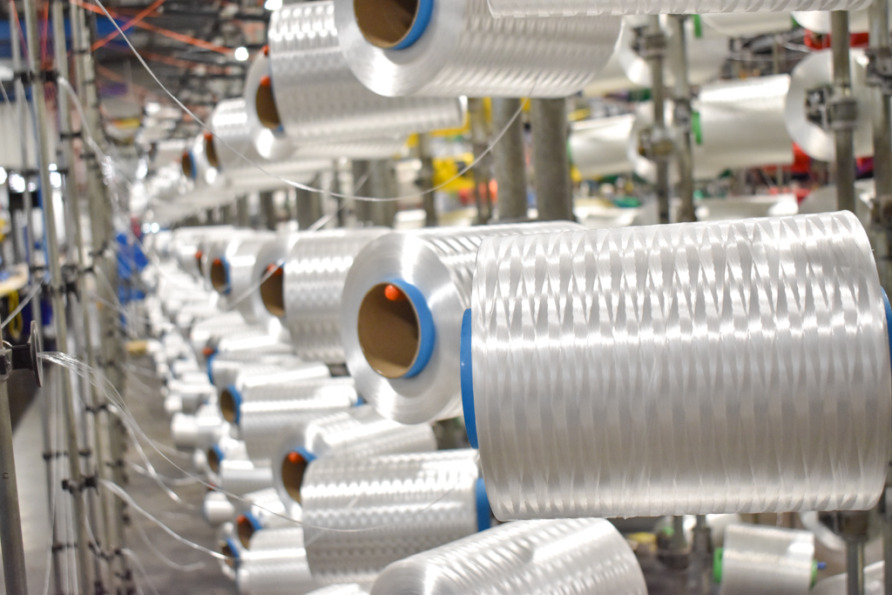 Spools of reflective white thread on industrial machinery in a textile manufacturing facility.